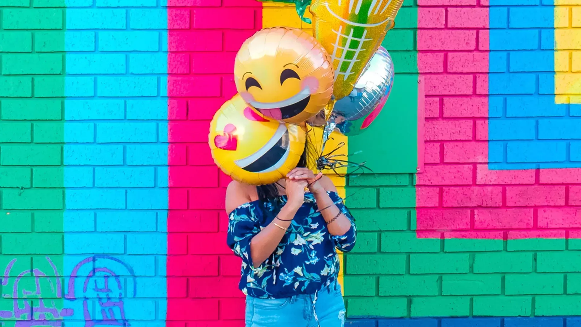 Una niña celebra su cumpleaños con globos frente a un colorido mural.