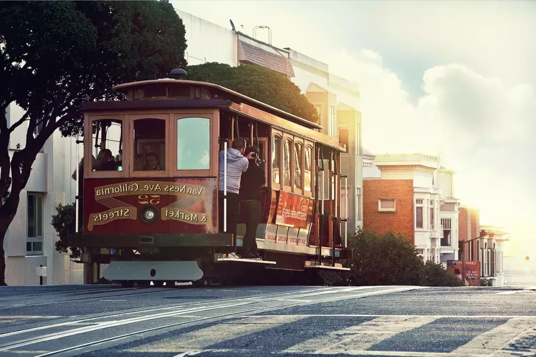 Un tram costeggia una collina a San Francisco, mentre i passeggeri guardano fuori dal finestrino.